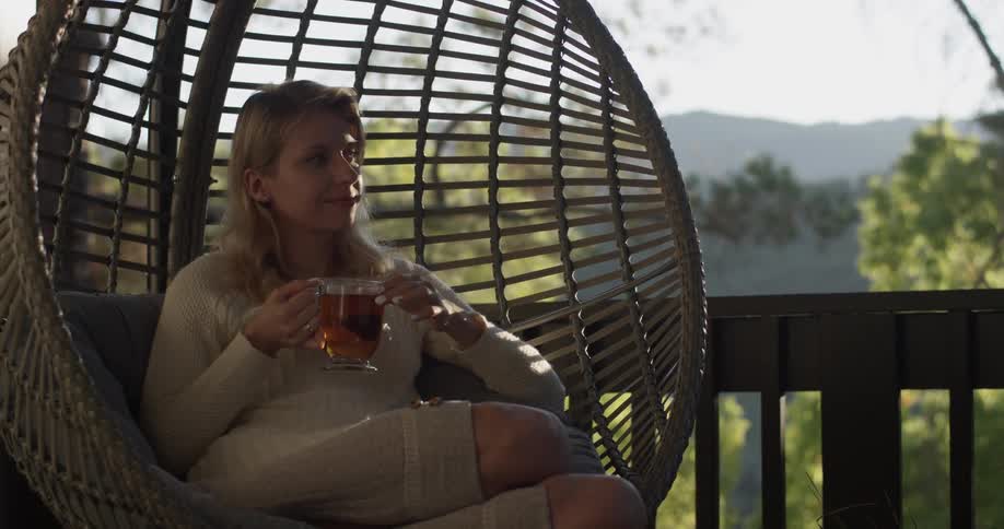 Woman sitting in a circular swing sips a mug of tea