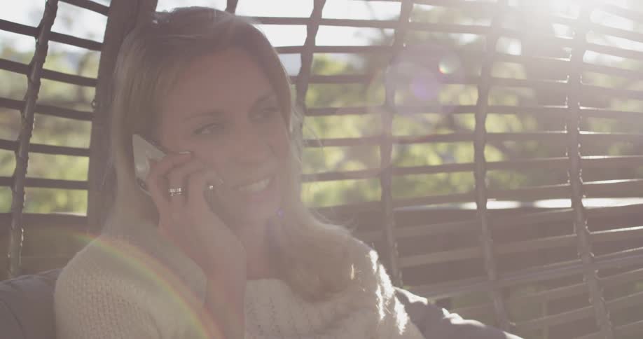A woman sitting on a swing, answers a phone call