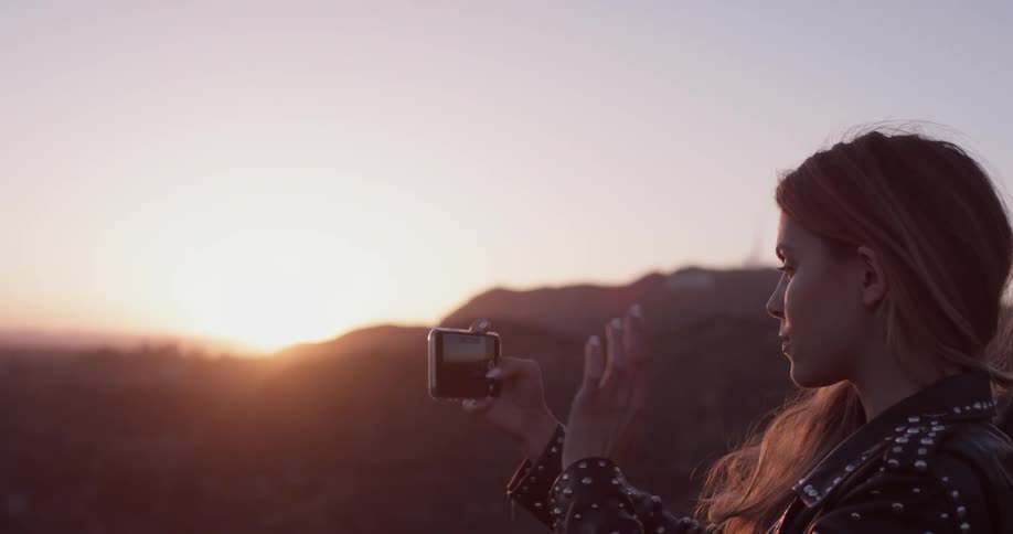A woman takes a photo with her phone as the sun sets
