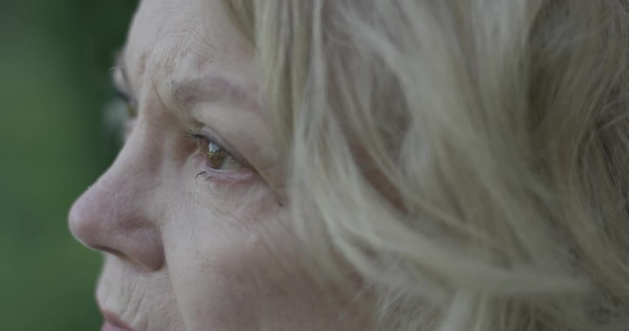 An older woman sits solemnly looking forward as she sits outside