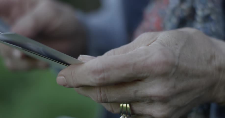 Hands of elderly person looking at photographs outdoors