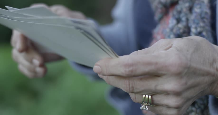 Elderly hands of a woman with wedding ring is holding papers and sorting through them reading them and sitting