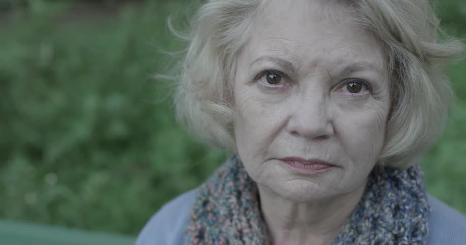 An old woman sits on a bench looking straight ahead