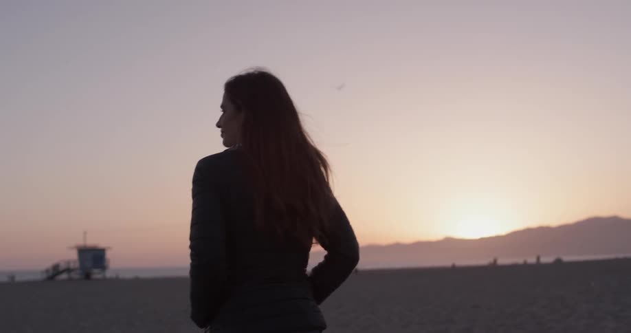 A woman is walking on the beach at sunset