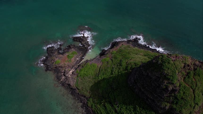 Water clashes into rocks on a small island with a large hill and grass and trees on a sunny day