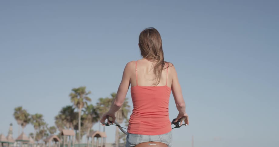 The backside and top half of a woman riding a bike with palm trees in the background