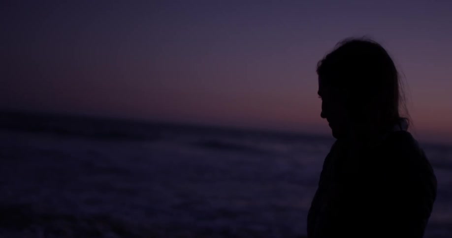 A woman walks on the beach in near darkness