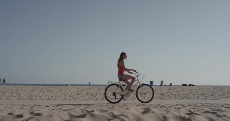 A woman rides a bike on a path that cuts through the beach with other cyclists