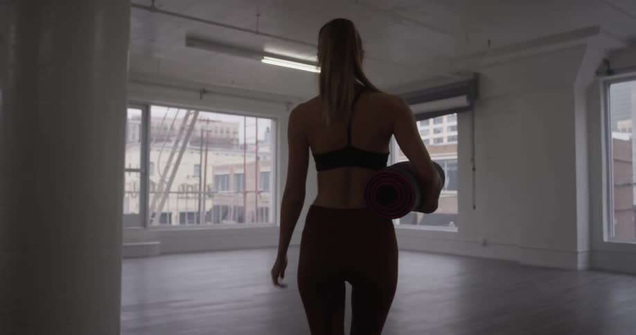 Woman carrying a yoga mat walks into an empty room