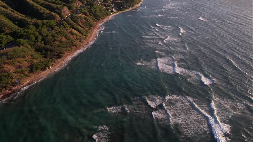 Waves breaking on a small beach by tree and shrub lined hills