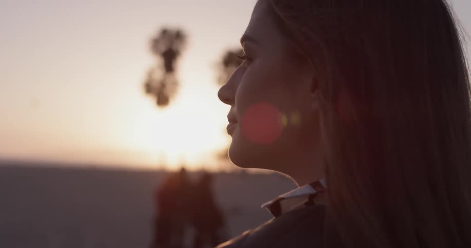 A woman looks into the distance as the sun sets brightly in front of her