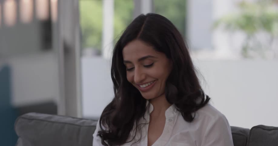 A woman with long beautiful hair wears a white shirt and virtual reality goggles which she takes off and is happy about her experience