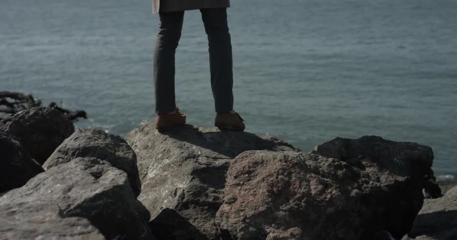 A person is standing on rocks near an ocean