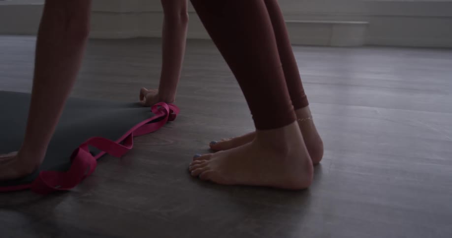 A closeup of a woman's feet rolling out a yoga mat and placing it on the floor
