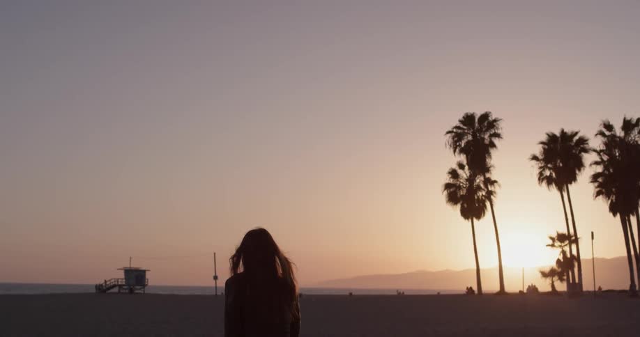 A woman is standing outside while the sun is setting