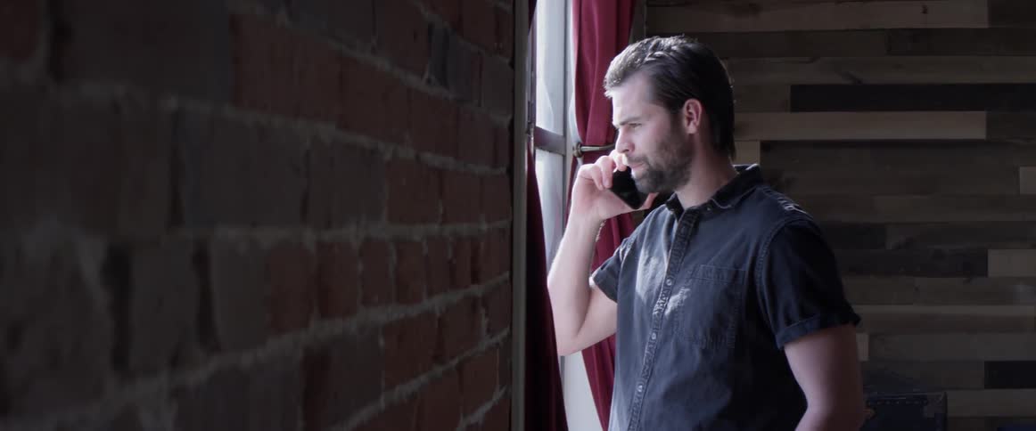 A man is talking on a phone by a window