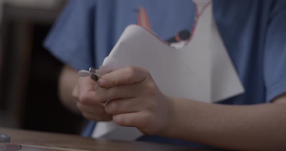 A child is cutting a corner of a piece of folded paper using a pair of scissors