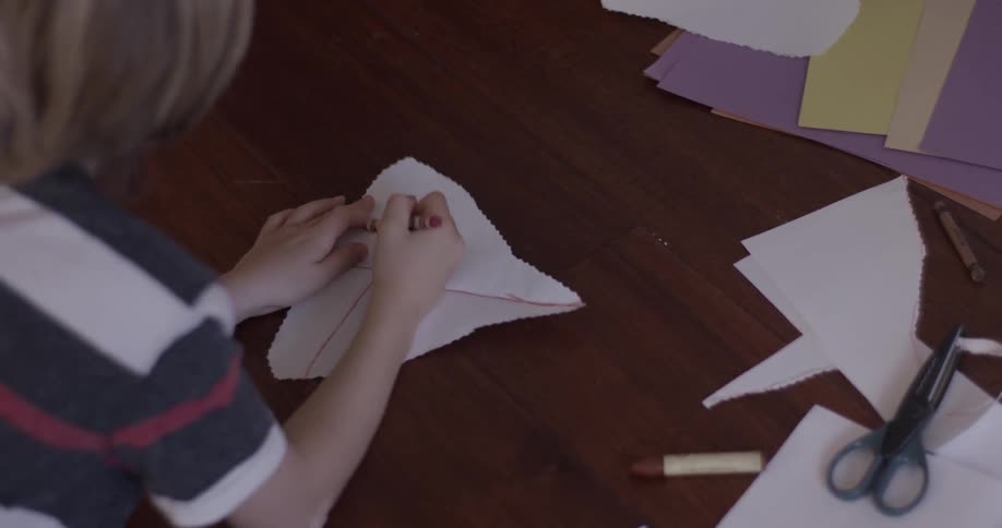 Child rests on the floor laying down and drawing shapes on a piece of paper he cut out