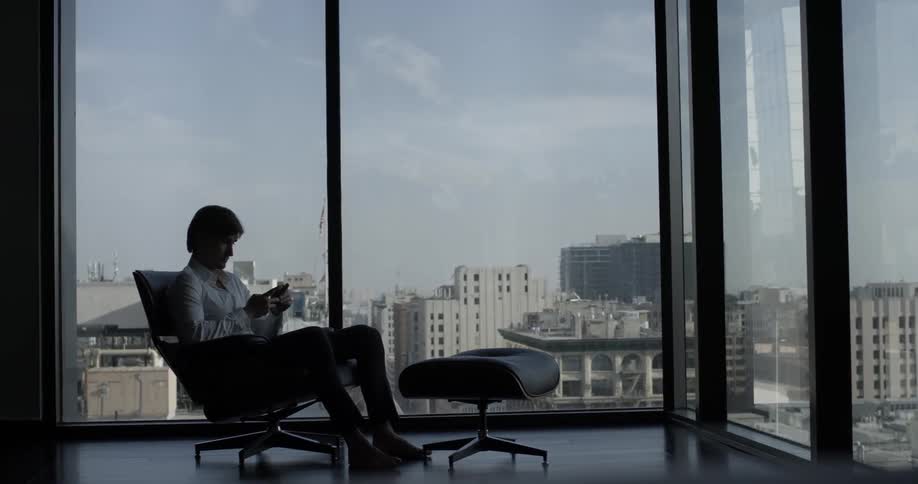 A man is sending a text while looking outside at the city