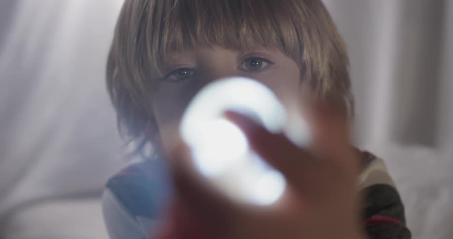 A boy shines a flashlight at a glass oval shaped object inside his tent