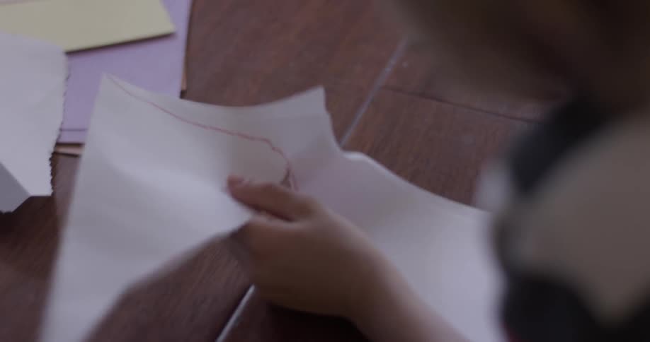A child sits at a table and cuts paper with jagged scissors following a line drawn on the paper