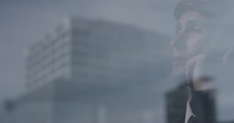 We see a man talking on his cellphone through a window with a reflection of the cityscape