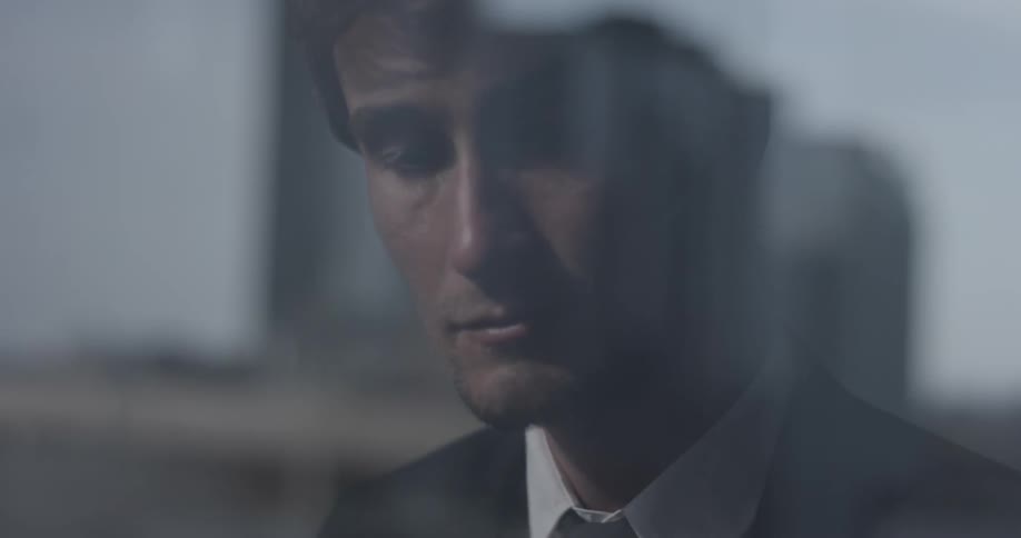 A young man can be seen in a suit through a window with a reflection of the city on a bright day