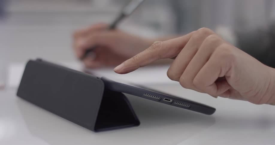 Closeup of a woman's hands writing and using a tablet