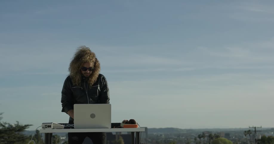 A man is outside with his laptop and piano doing a performance