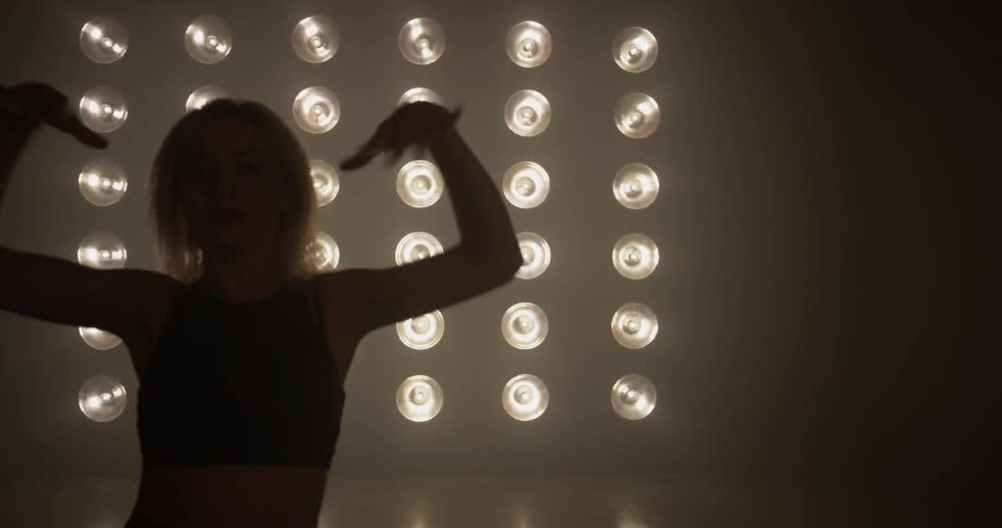 A woman is dancing in a dark room with bright lights behind her
