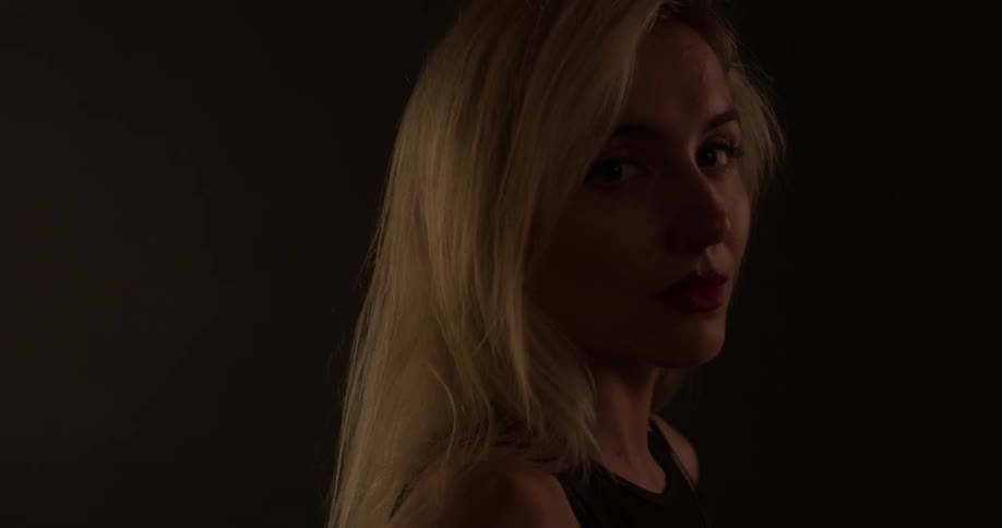 A blonde woman looks up and towards the camera with a sultry expression