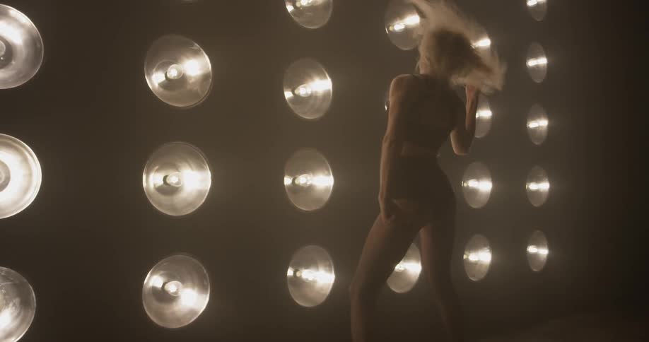 A dark room with large light bulbs shine on a woman dancing