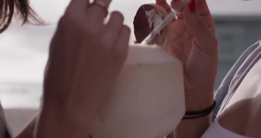 Two women drink out of a coconut from straws