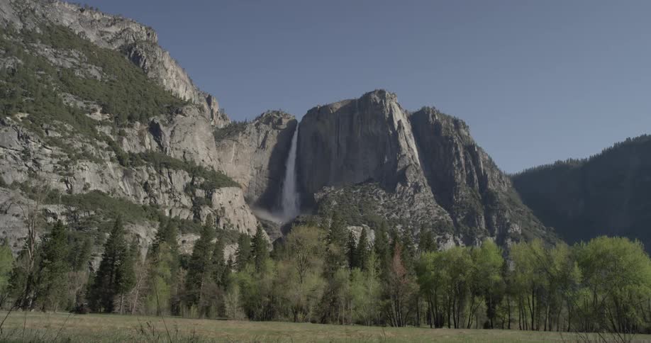 A waterfall flows off the side of a cliff that has a layer of trees in front of it