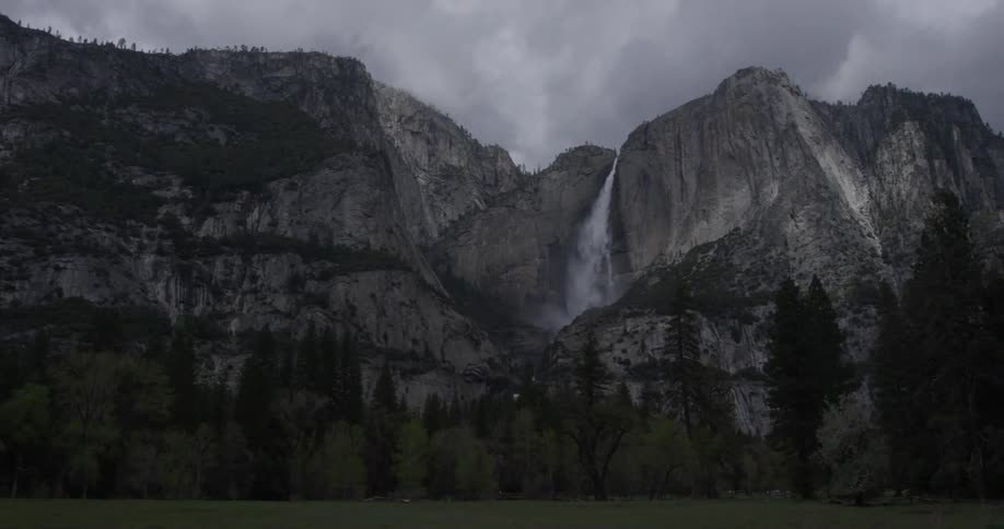 Water flows off the side of a mountain into the valley below where many trees are standing