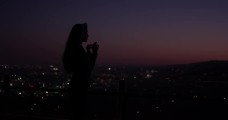 Woman puts headphones on at night with a city below