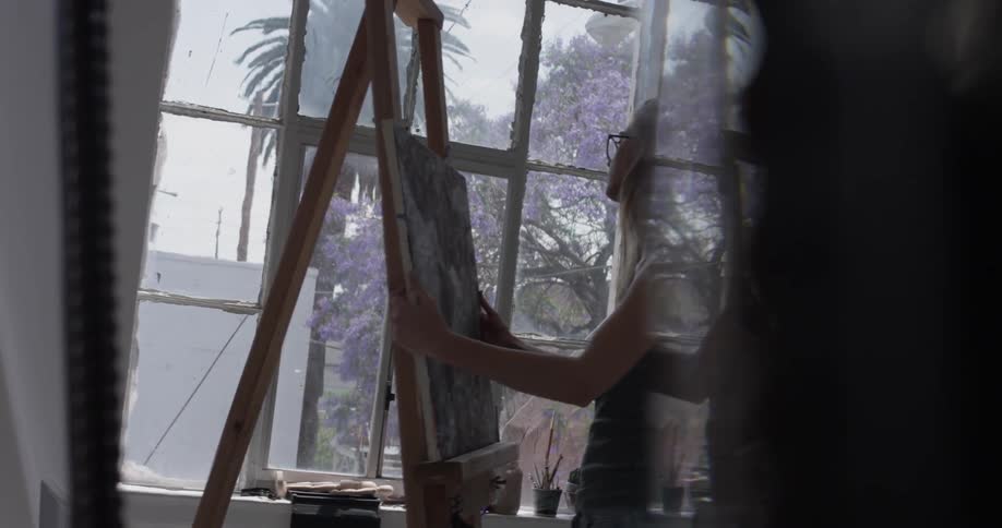 A woman placing a painting on an easel