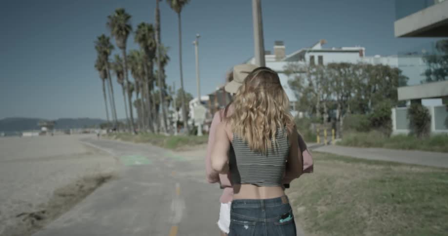 Two women ride a scooter together by the beach