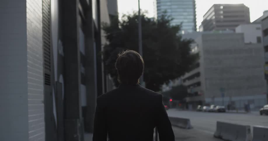 Man wearing a suit walking down a city street with cars driving by