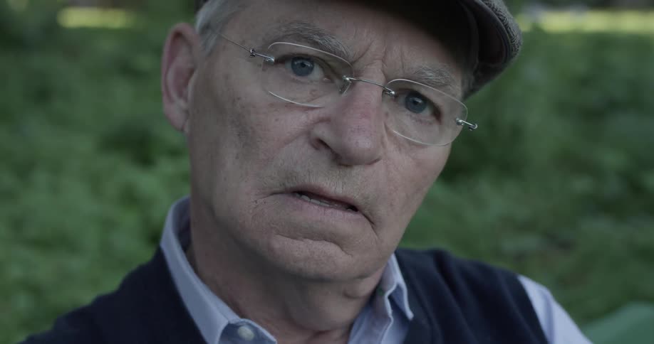 Elderly man sitting on bench at park looking grumpy