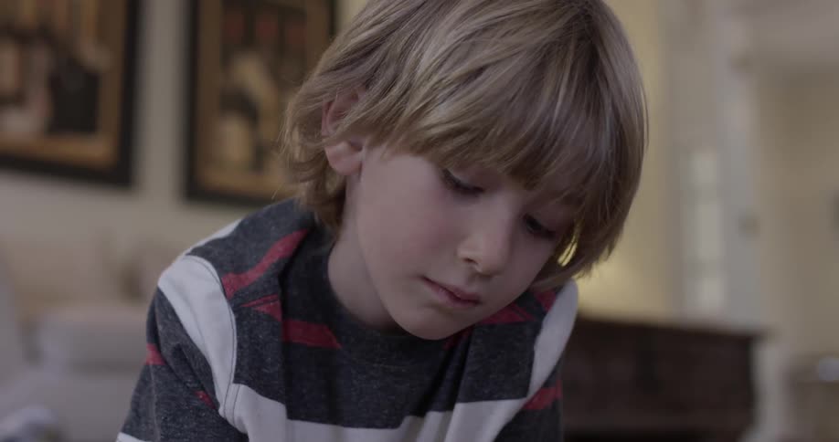 A child lays on the floor with a black and white red striped shirt observing something below