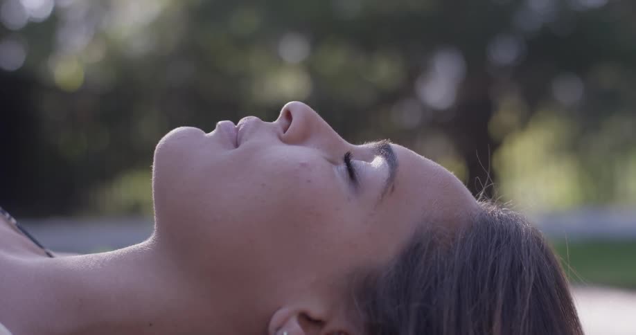 A woman lays on her back with her eyes closed near trees