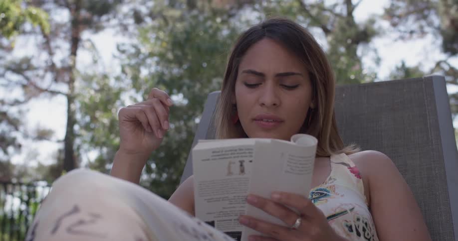 A woman sits in a chair outside and reads a book