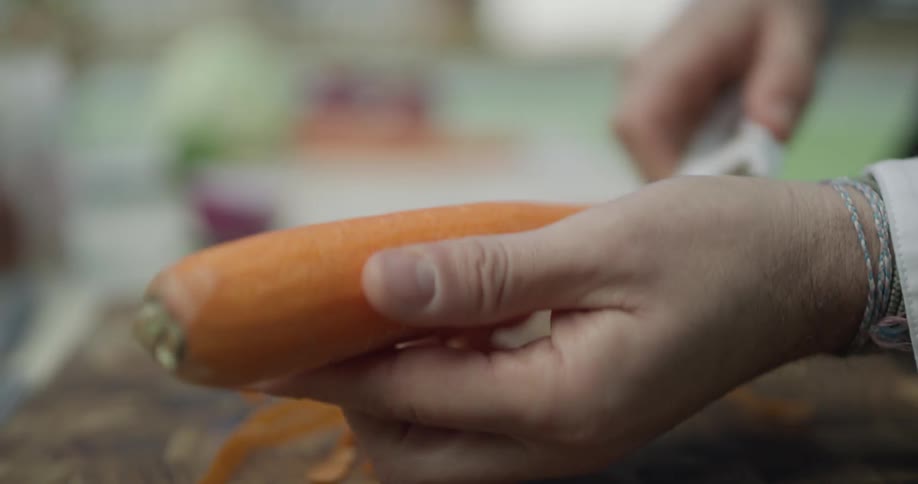 Man peels a carrot over a cutting board on a sunny day