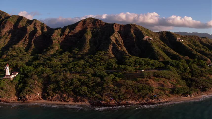 Ocean waves alongside rolling green tree lined hills