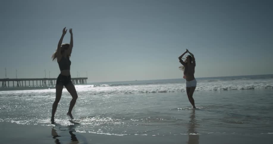 Woman performs a flip on the beach and celebrates with another woman