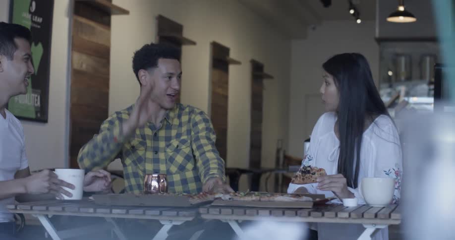 Two men and a woman sitting at a table eating pizza high five each other