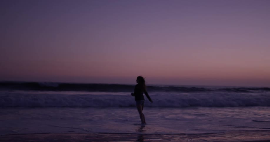 Woman playfully walks in the surf at dusk