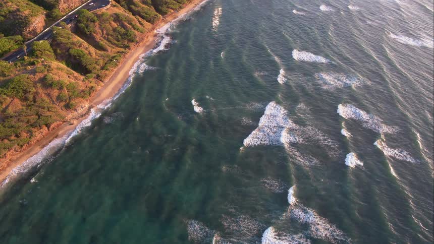 Waves stream towards the shore that has a road running along it