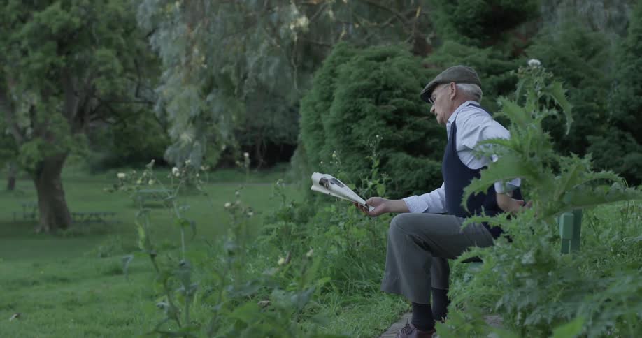 Man outside is sitting on bench reading